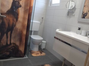 Une salle de bain comprenant des toilettes, un lavabo, un miroir et un espace douche.