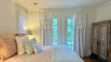 A bedroom with a bed, curtains, a lamp, and a view of greenery outside.