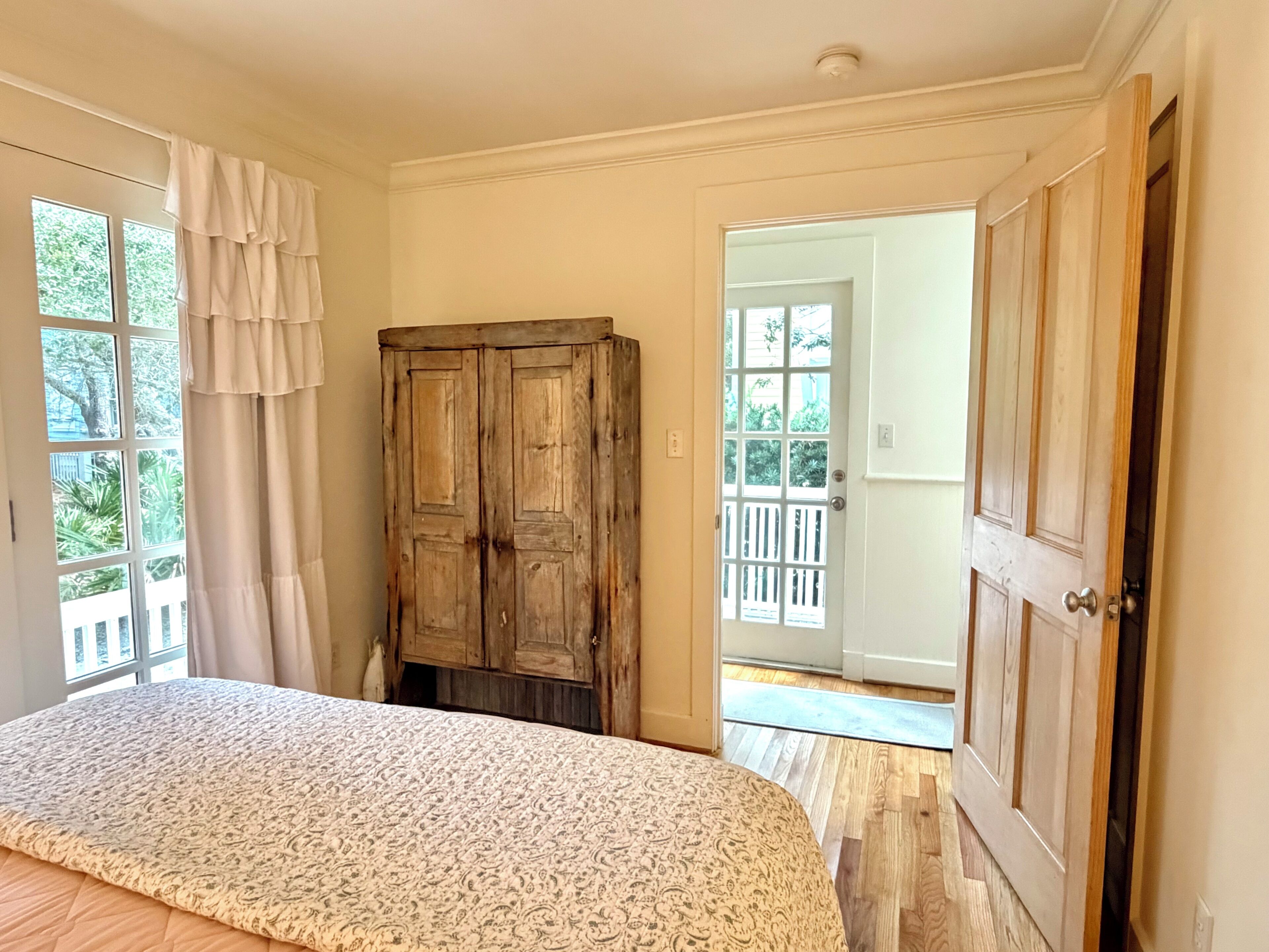 Une chambre à coucher comprenant un lit, une armoire en bois, une porte donnant sur un balcon extérieur et une fenêtre avec des rideaux.