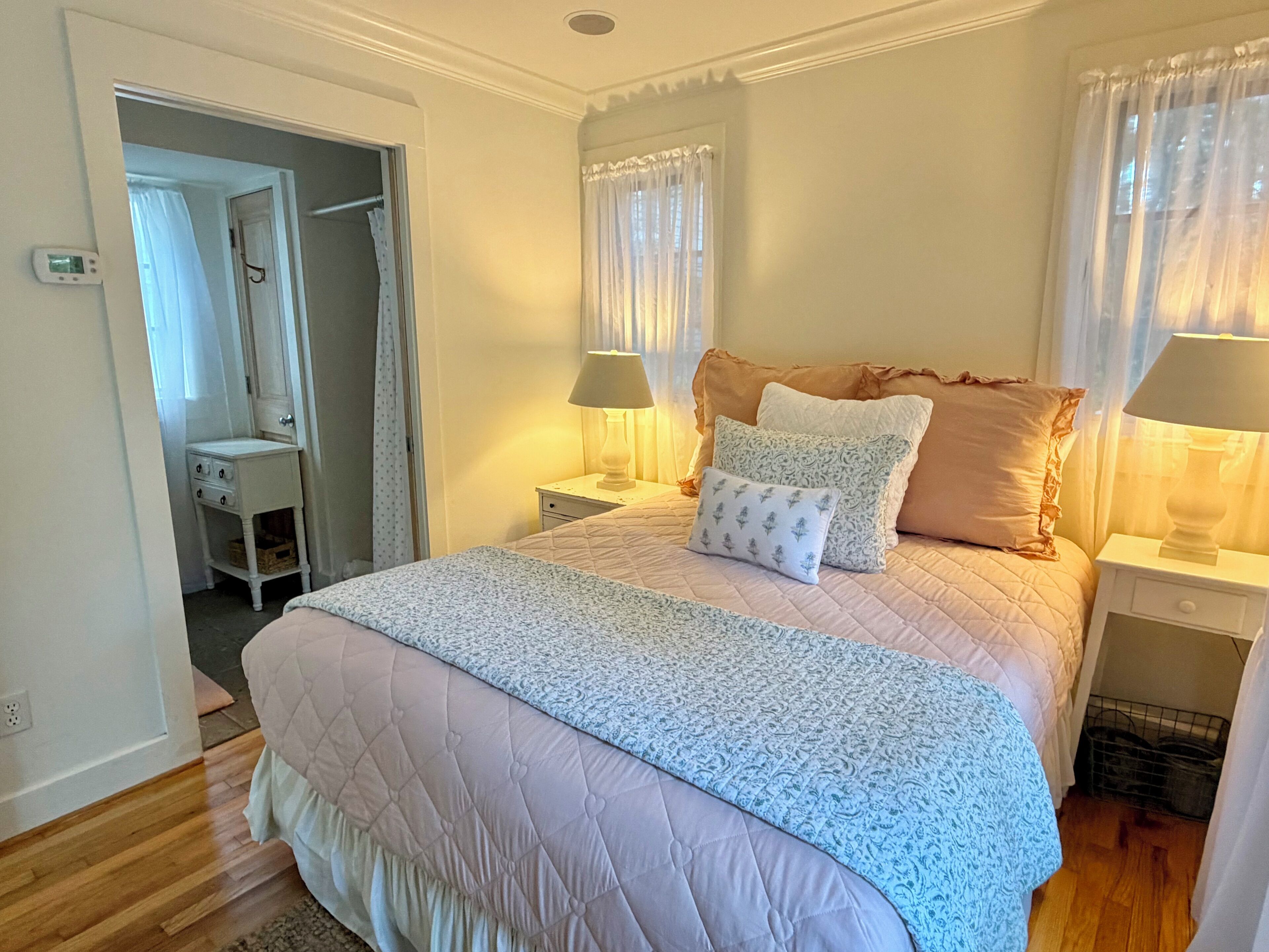 A bedroom with a bed, two bedside tables, a nightstand, a mirror, and a door leading to a bathroom.