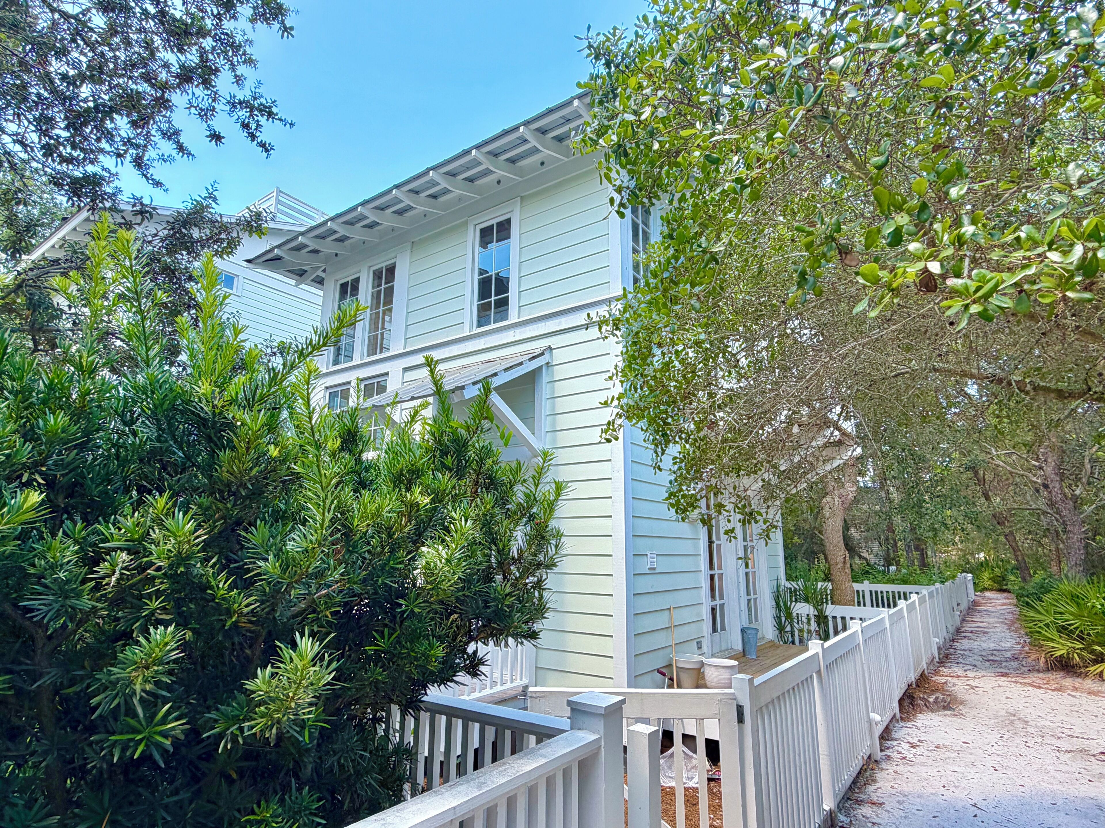 A two-story house with a white exterior, surrounded by dense greenery and a wooden deck.