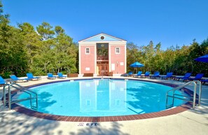 Una piscina con un edificio rojo al fondo, rodeada de sillas de descanso y sombrillas azules.