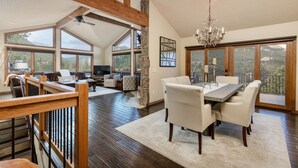 A spacious living area with a large window, a fireplace, and a dining area with a chandelier. - Alpenglow Vacation Home At Windcliff 4 Bedroom Home by RedAwning (Estes Park)
