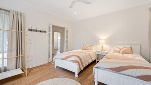 Quarto com duas camas, um ventilador de teto e piso de madeira.