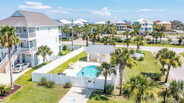 A multi-story building with a pool, surrounded by palm trees and a white fence.