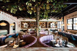 Un restaurante con mesas redondas, asientos acolchados morados y un gran árbol en el centro.