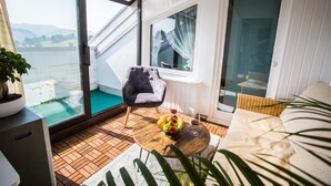 Ein Balkon mit Meerblick, ein Korbstuhl, ein Holztisch mit Obst und Wein sowie eine Couch.
