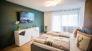 Ein modernes Schlafzimmer mit einem Bett, einer weißen Kommode, einem an der Wand montierten Fernseher und einem Fenster mit Vorhängen.