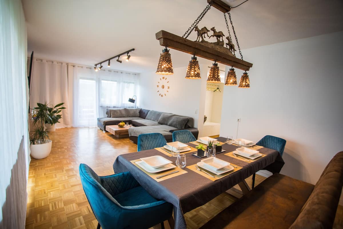 Un comedor con una mesa larga dispuesta para cuatro personas, rodeada de sillas tapizadas en azul.