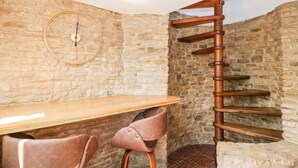A rustic stone-walled room with a wooden table, two leather chairs, a round wall clock, and a spiral staircase. - Steel Works Farm (Ross-on-Wye)