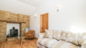 A cozy living room with a stone fireplace, a wooden door, and a sofa with floral cushions. - Steel Works Farm (Ross-on-Wye)
