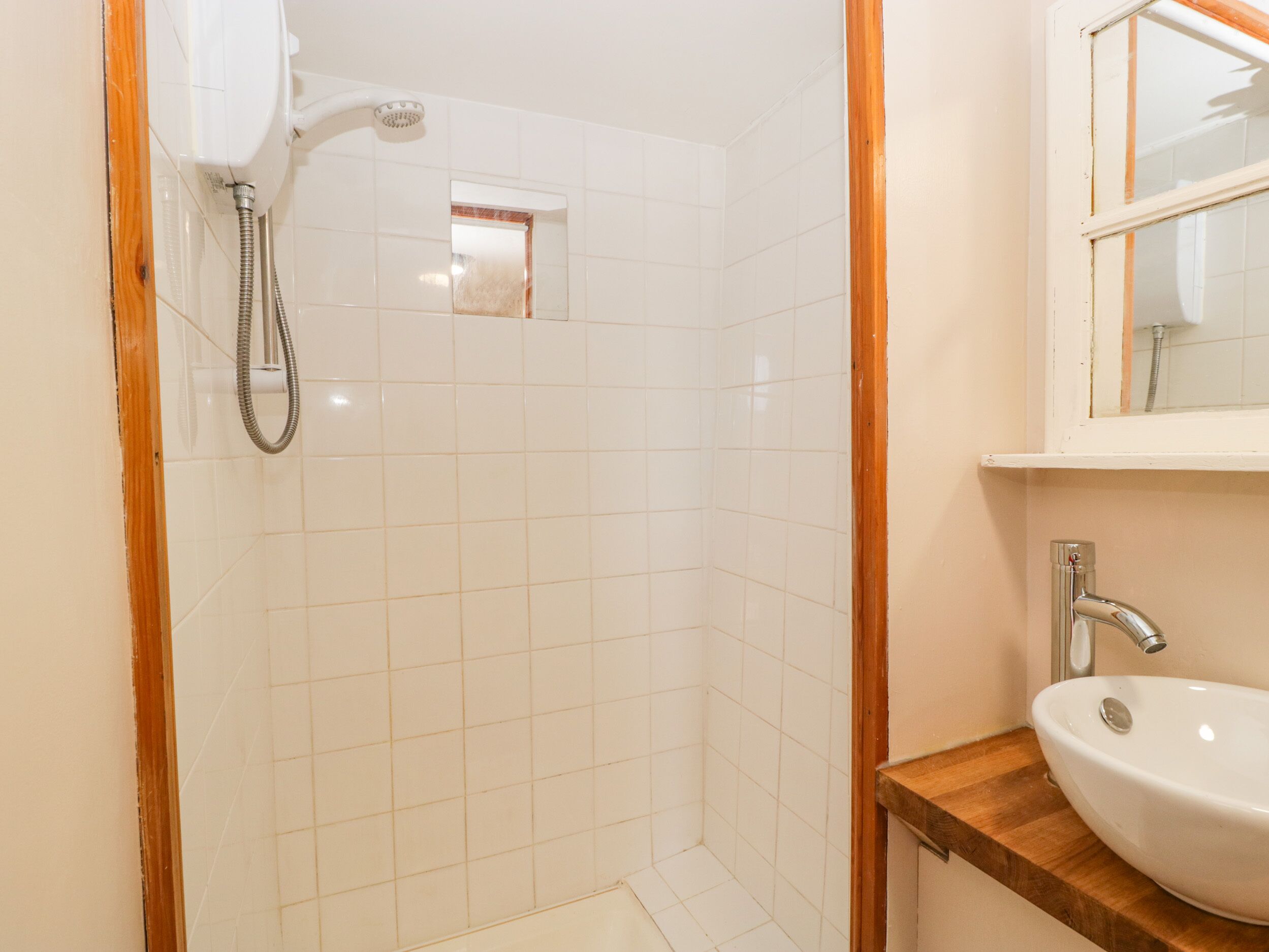 A bathroom with white tiled walls, a wooden-framed shower enclosure, and a wooden countertop with a white sink.