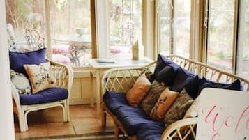 A sunroom with a ceiling fan, wicker furniture, and a 'Welcome Home' sign.