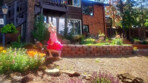 A two-story house with a balcony, surrounded by a garden with various plants and flowers. - Cabin's entire, private lower level w/ mountain view & cozy, comfortable living. (Colorado Springs)