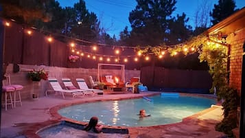 A backyard with a swimming pool, lounge chairs, and string lights.