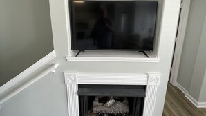 Een open haard met een televisie erboven, een bovenkant met decoratieve objecten, en een trap die omhoog leidt.