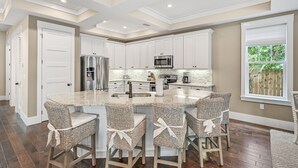 A modern kitchen with white cabinetry, a central island with bar stools, stainless steel appliances, and a view of the outdoors. - Private Pool, Pet Friendly, and Beach Access- Sea-Rest by Royal Destinations (Inlet Beach)