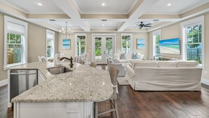 A spacious kitchen with a granite countertop, a dining area with a white table and chairs, and a large white sofa in a bright living room with large windows and ceiling fans. - Private Pool, Pet Friendly, and Beach Access- Sea-Rest by Royal Destinations (Inlet Beach)