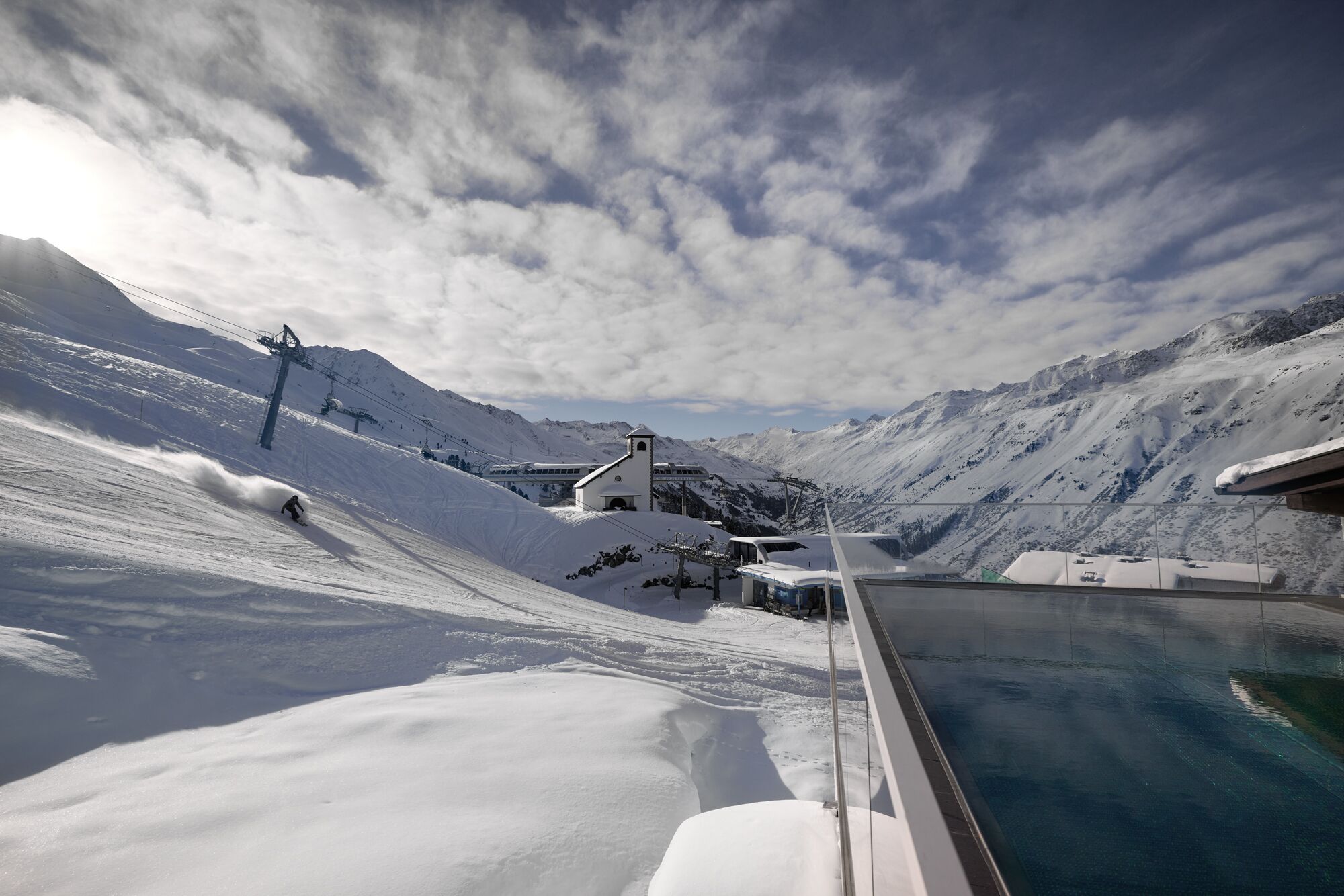 A snow-covered mountain landscape with a ski lift, a small building, and a pool area.