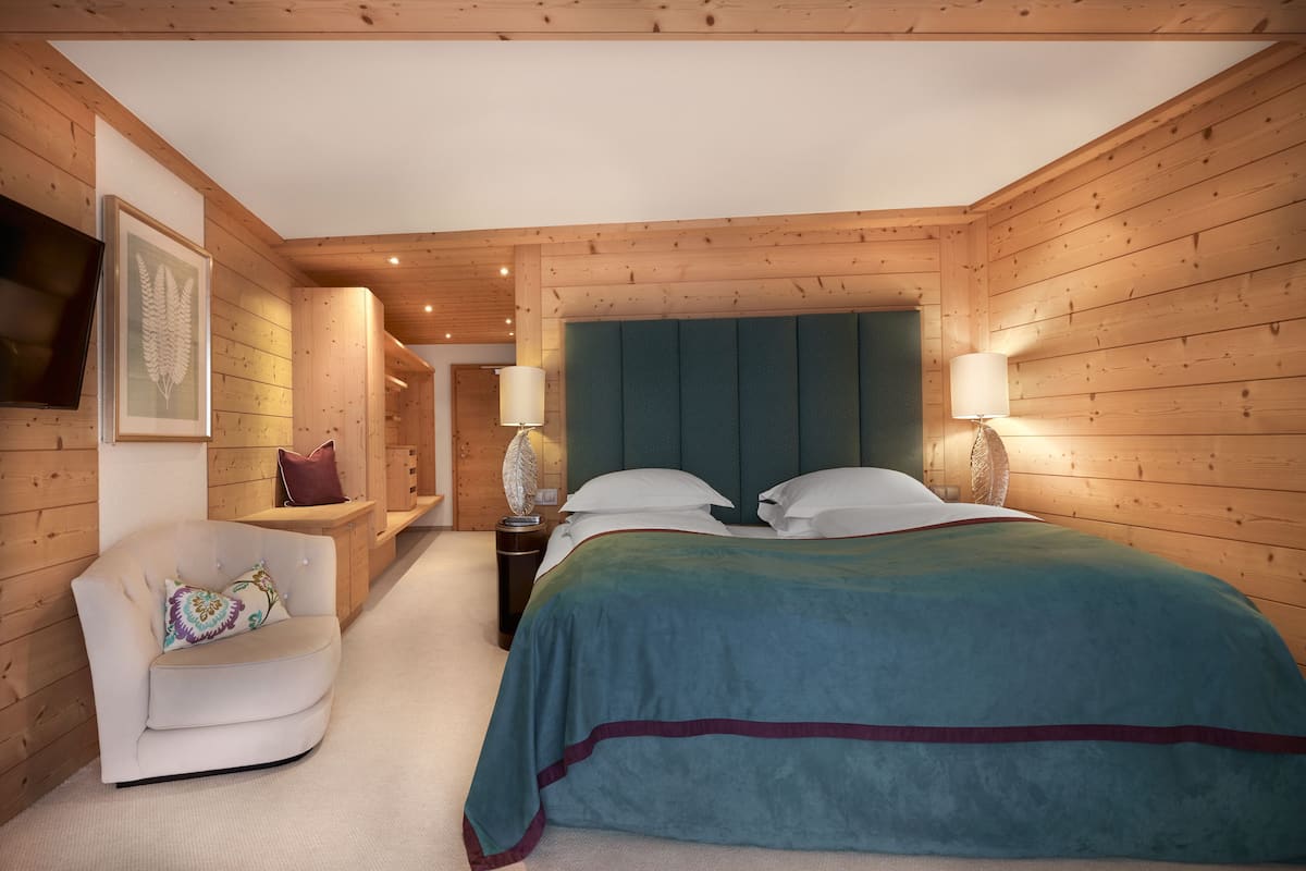 Un dormitorio con paredes de madera, una cama con colcha color turquesa, un sillón blanco y un televisor montado.