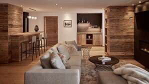 A modern living room with a sofa, coffee table, and a fireplace. There is a kitchen area with wooden cabinets and a bar counter.