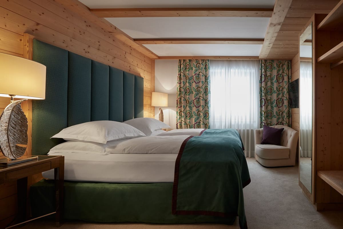 Habitación de hotel con una cama grande, cabecera de madera, escritorio con lámpara, una silla y televisor en la pared.