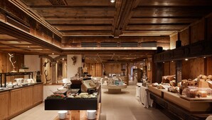 A spacious, wooden-floored restaurant with a central buffet area, wooden beams on the ceiling, and various food items displayed.
