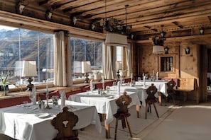 A dining area with multiple tables set for a meal, large windows offering a view of the mountains, and wooden ceiling beams. - Top Hotel Hochgurgl (Soelden)