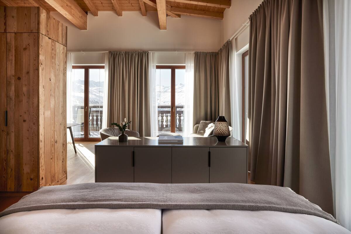 Un dormitorio con una cama grande, paredes de madera, un aparador y vistas a montañas a través de las ventanas.
