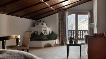 A cozy room with a wooden ceiling, a sofa, a chair, a table, and a view of mountains through a large window.