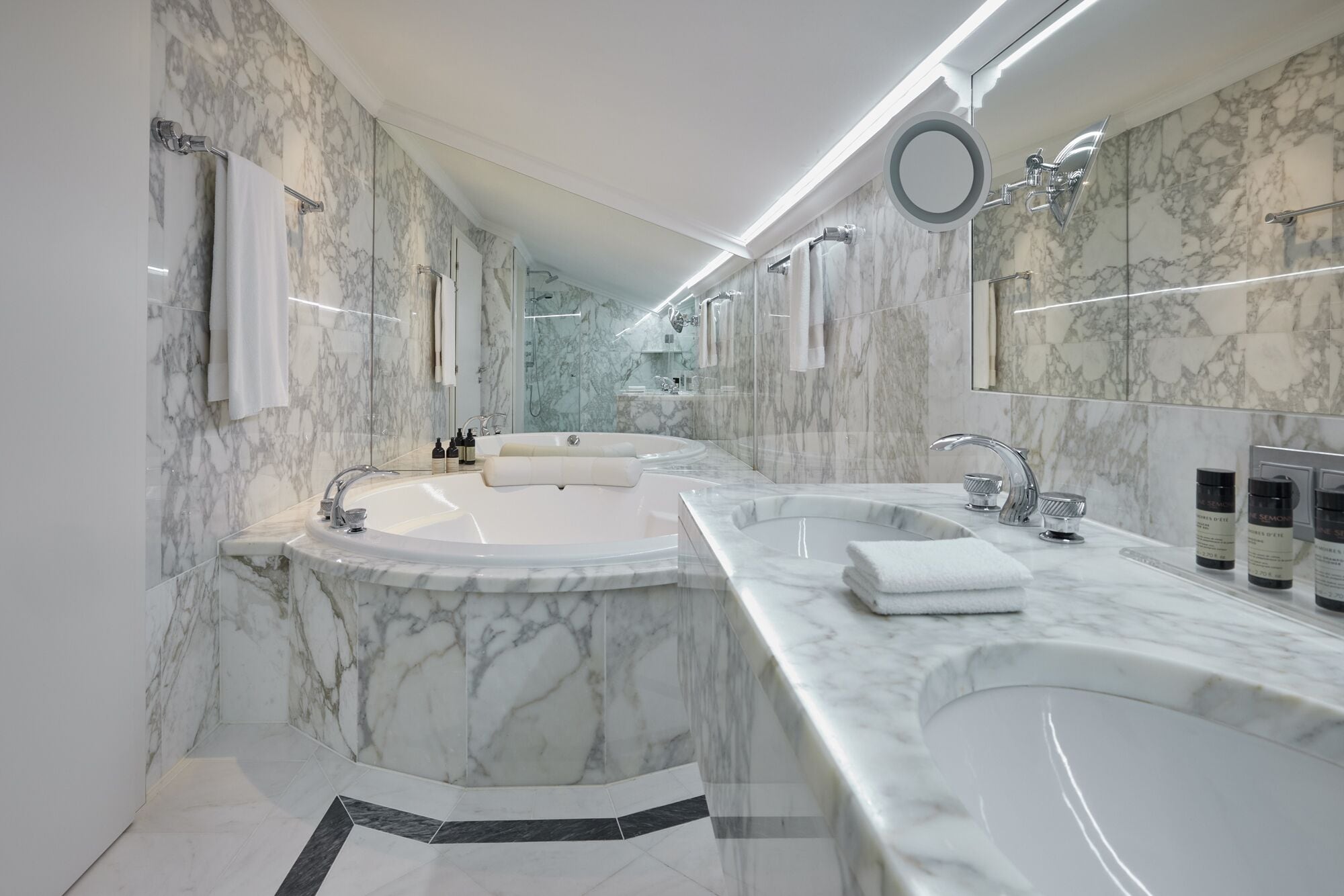 Une salle de bain moderne avec des murs en marbre, une grande baignoire et un espace lavabo séparé.