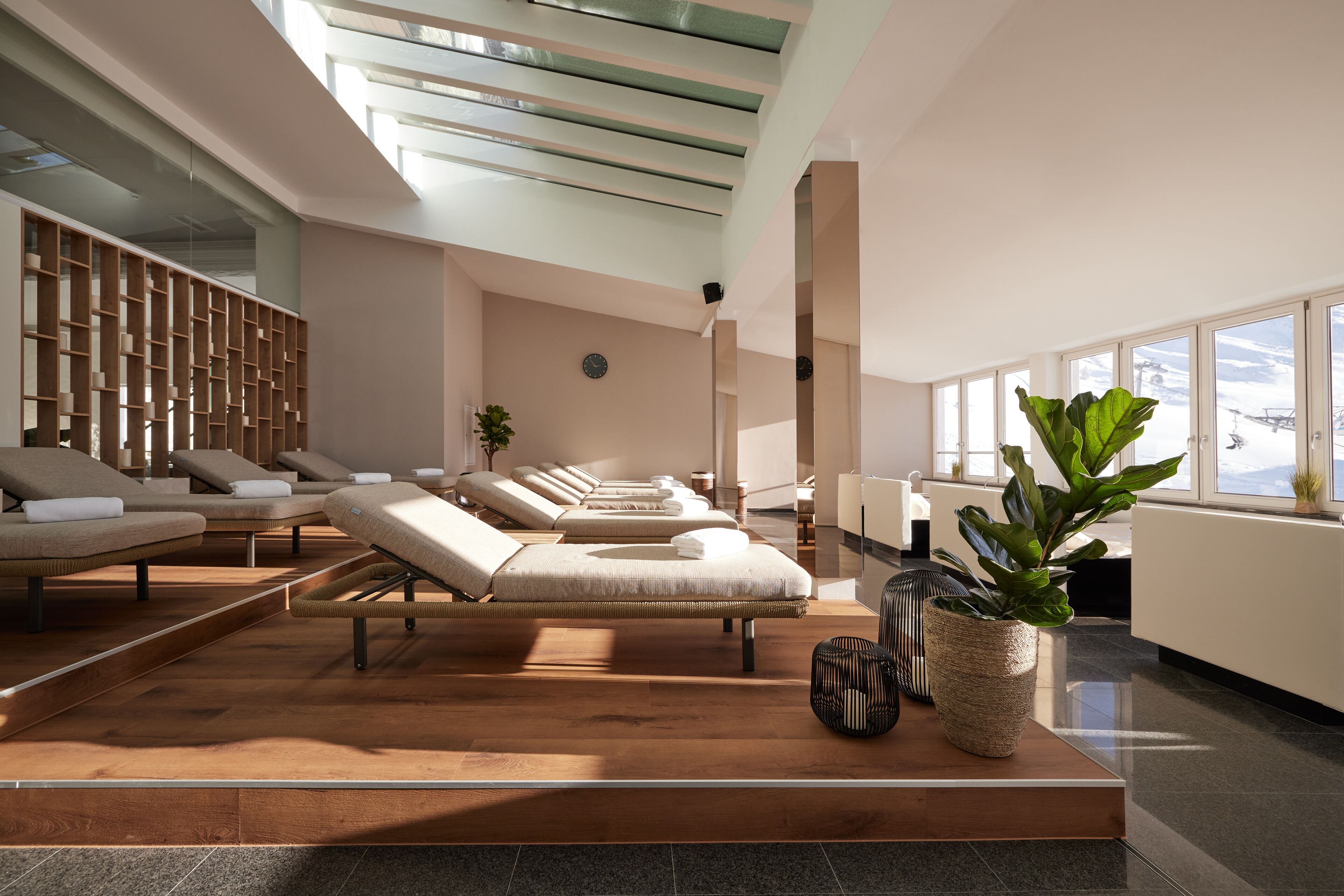 A modern spa area with multiple massage tables arranged in a row, a reception desk, and large windows providing natural light.