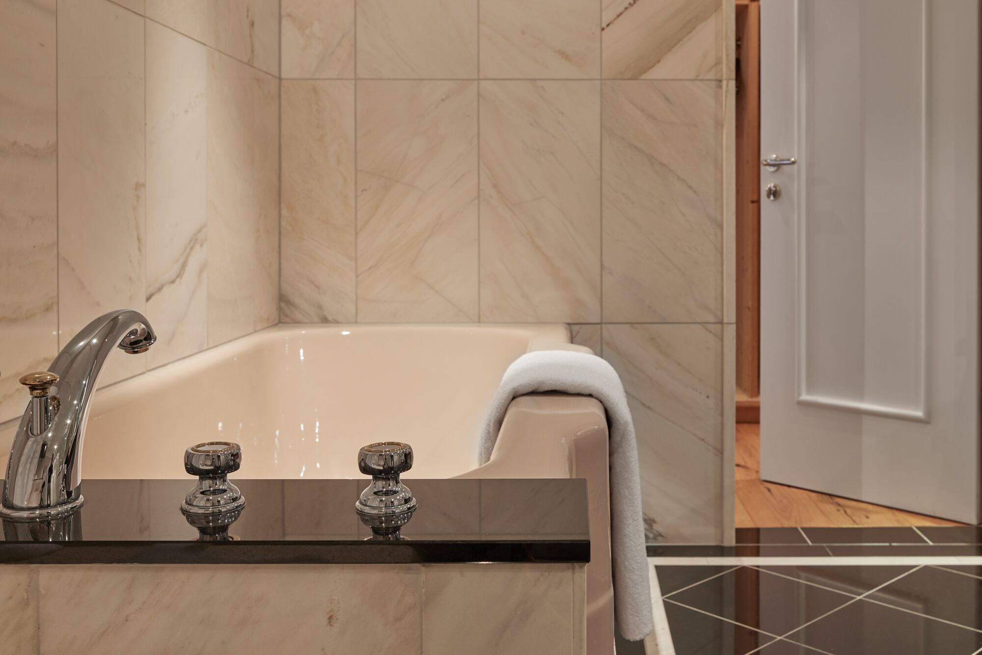 Ein Badezimmer mit einer Badewanne, einem Waschbecken mit zwei Wasserhähnen und einem Handtuch am Rand.