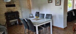 Un coin repas avec une table blanche et des chaises noires, une cheminée et des tableaux encadrés au mur.