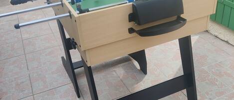 Une table de baby-foot dotée d’un tiroir pour ranger les balles, posée sur un sol carrelé.
