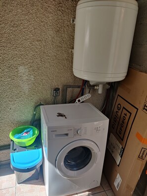 Eine Waschmaschine, ein Wassertank und ein grüner Korb mit blauem Deckel.