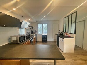 A compact kitchen with a microwave, stove, and sink. There is a window providing natural light and a view of the outside. - House located in a quiet area, close to the town center. (Guidel)