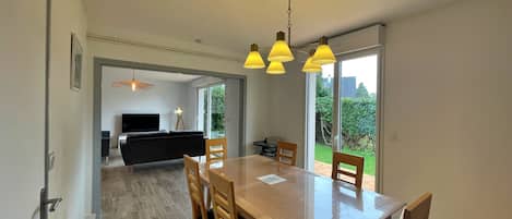 Un comedor moderno con una mesa y sillas de madera, una araña y vistas a un jardín a través de puertas correderas amplias.