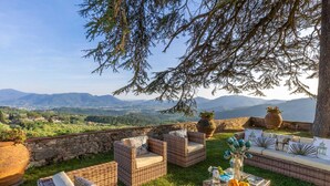Eine Terrasse mit Korbmöbeln, einer Steinmauer und Blick auf ferne Berge.