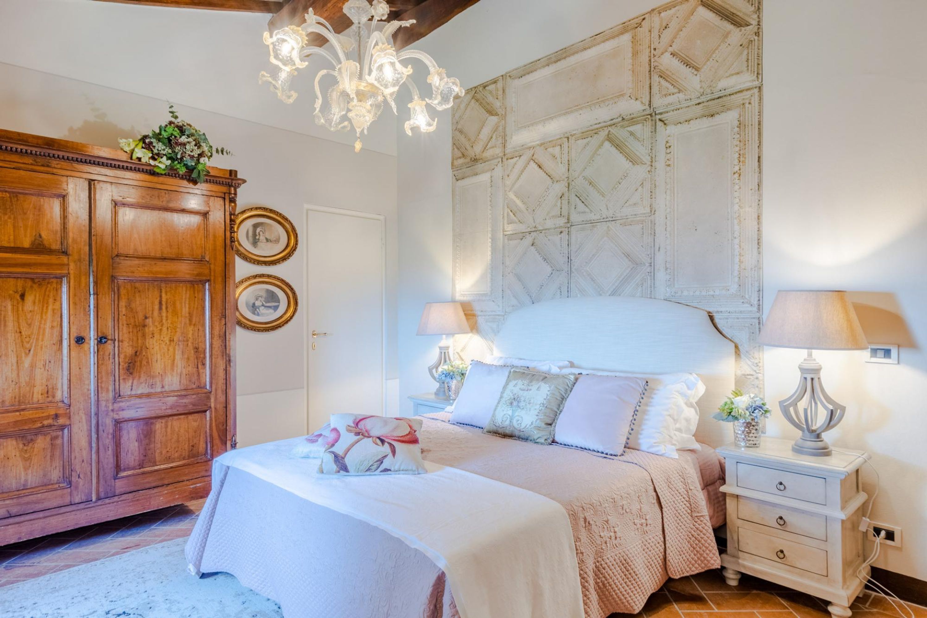 Une chambre avec une grande armoire en bois, un lit avec une tête de lit blanche, deux lampes de chevet et un lustre.