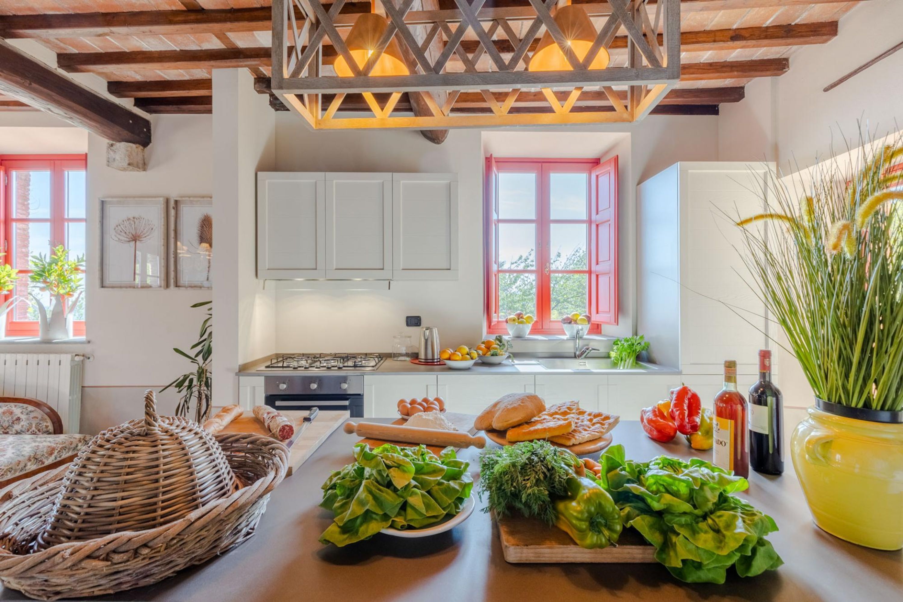A kitchen with white cabinets, a red window, and various fresh vegetables on the counter.