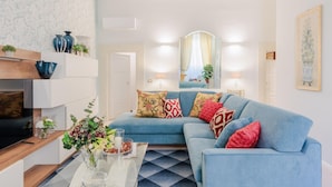 A modern living room with a blue sofa, decorative pillows, a glass coffee table, and a TV. - The Silk Thread the Luxury 3 Bedrooms Apartment (Lucca)