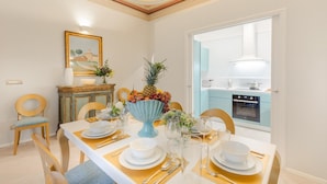 A dining room with a white table set for four, a blue vase with fruit, and a view of the kitchen through an open door. - The Silk Thread the Luxury 3 Bedrooms Apartment (Lucca)