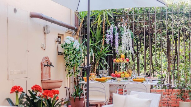 Une terrasse extérieure avec une table dressée pour le repas, entourée de plantes en pot et d’une variété de fruits et de légumes.
