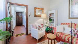 Un salon avec un canapé, un fauteuil et une table basse. On y trouve une porte qui donne sur une autre pièce, une lampe et un tableau encadré accroché au mur.