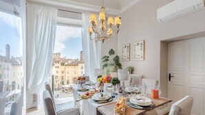 Zona pranzo con tavolo imbandito per quattro persone, un lampadario e vista sulla città attraverso ampie finestre.