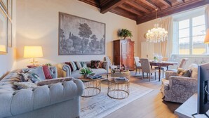 Un soggiorno con divano, poltrone, tavolino, televisore, lampadario e un quadro appeso al muro.