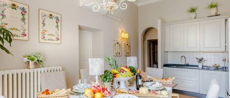 A well-lit dining area with a chandelier, white cabinets, and a fruit centerpiece on the table.