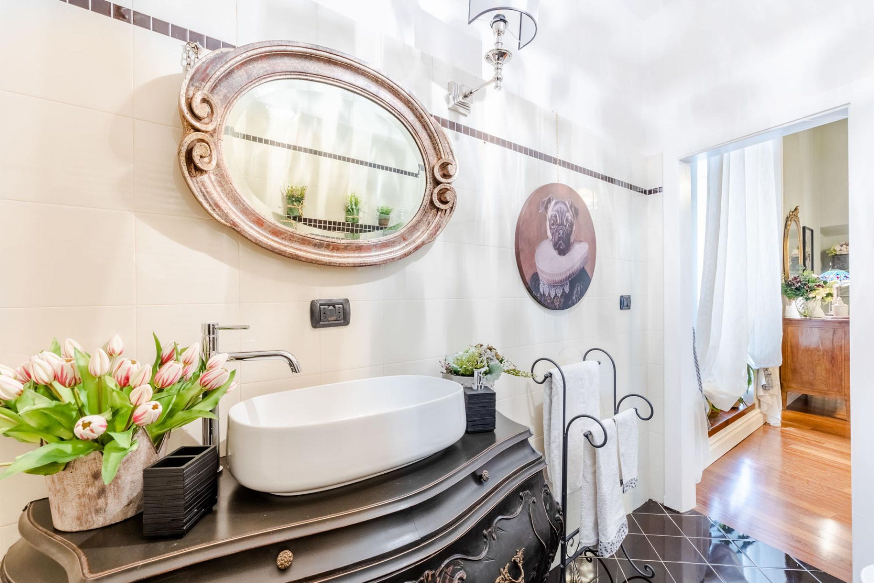 A bathroom with a white sink, a mirror with an ornate frame, a potted plant, and a towel rack.