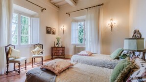 Un dormitorio con dos camas, un aparador, una silla y una ventana con cortinas.